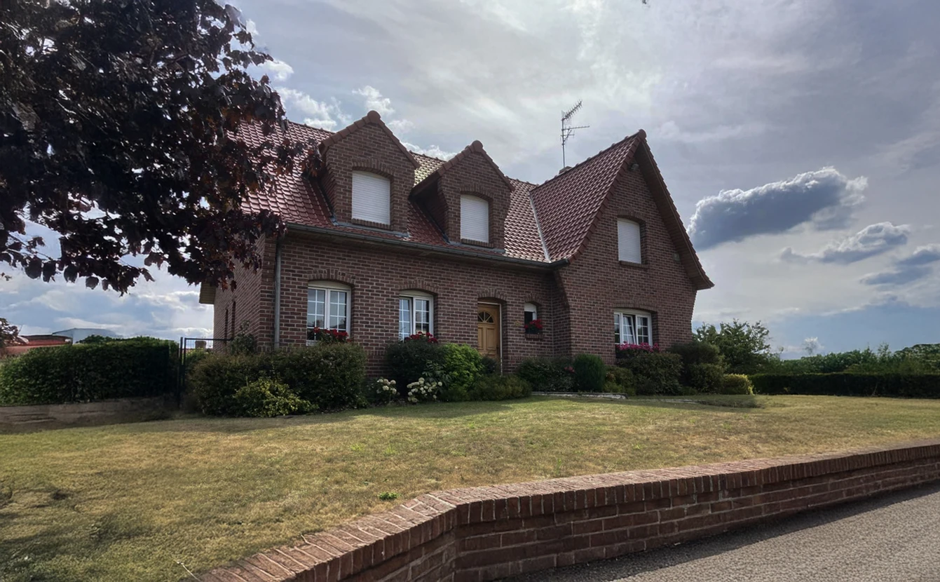 Maison individuelle en briques rouges avec toiture en tuiles terre cuite, située dans un quartier résidentiel