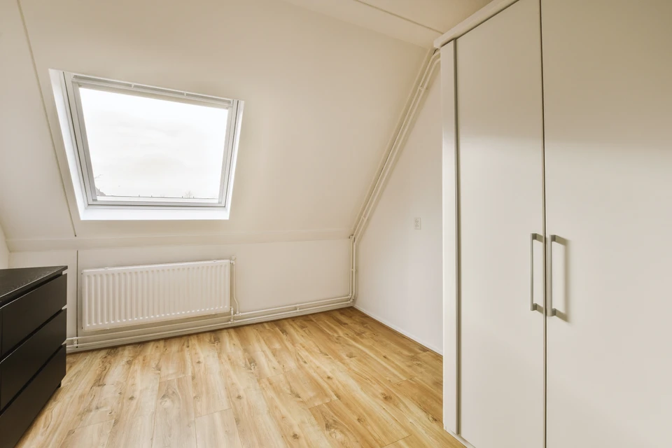 Ouvrier en combinaison bleue avec masque respiratoire N95 et gants blancs installe de l'isolant en laine minérale entre chevrons de charpente